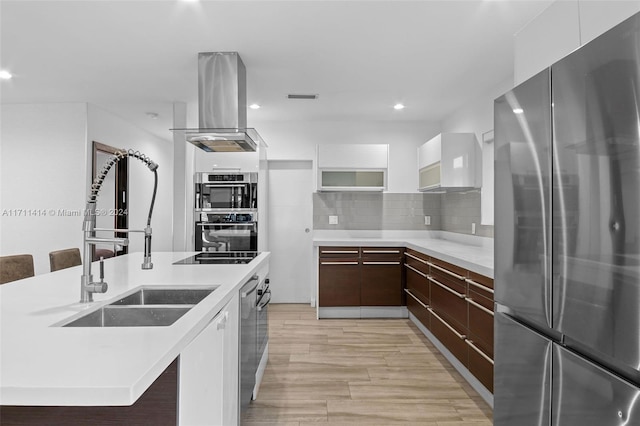 kitchen with appliances with stainless steel finishes, tasteful backsplash, sink, island exhaust hood, and wall chimney range hood