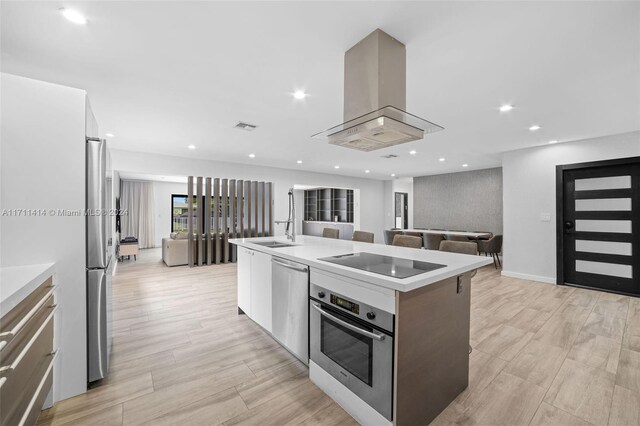 kitchen featuring white cabinetry, an island with sink, island exhaust hood, stainless steel appliances, and light wood-type flooring