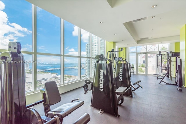 workout area featuring expansive windows, a water view, and french doors