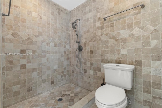 bathroom featuring tiled shower, toilet, and tile walls