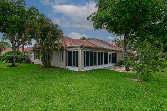 rear view of house featuring a lawn, a sunroom, and central AC