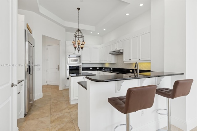 kitchen featuring hanging light fixtures, light tile patterned floors, a raised ceiling, a breakfast bar, and white cabinets