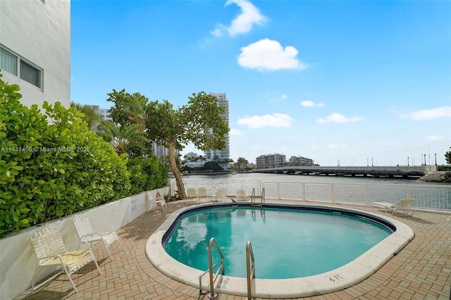 community pool with a water view, a patio area, and fence