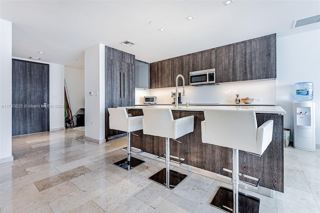 kitchen with a breakfast bar, dark brown cabinets, a center island with sink, and sink