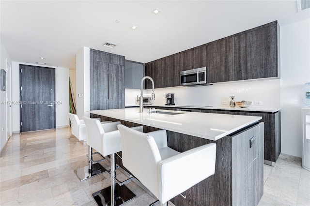 kitchen with a kitchen breakfast bar, a center island with sink, dark brown cabinets, and sink