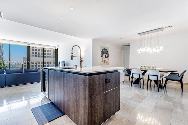 kitchen featuring pendant lighting, expansive windows, sink, an island with sink, and dark brown cabinets