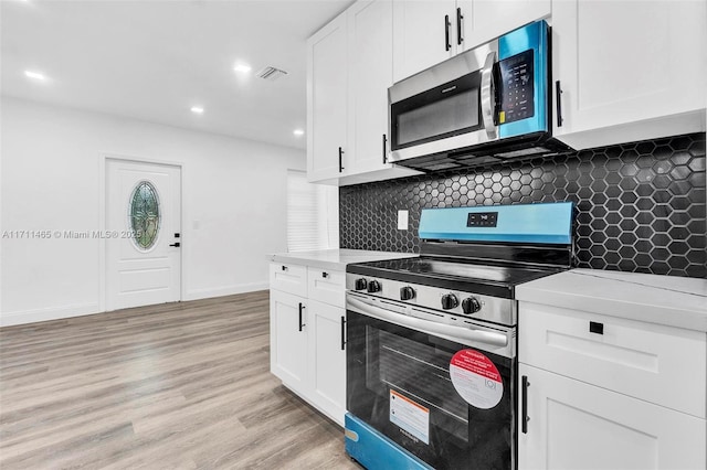 kitchen with decorative backsplash, white cabinetry, light hardwood / wood-style floors, and appliances with stainless steel finishes