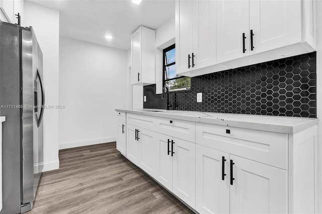 kitchen with tasteful backsplash, sink, hardwood / wood-style flooring, stainless steel fridge with ice dispenser, and white cabinetry