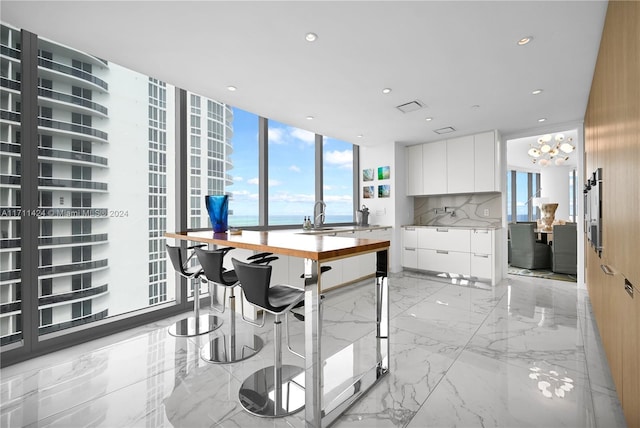 kitchen with tasteful backsplash, sink, a water view, a wall of windows, and white cabinetry