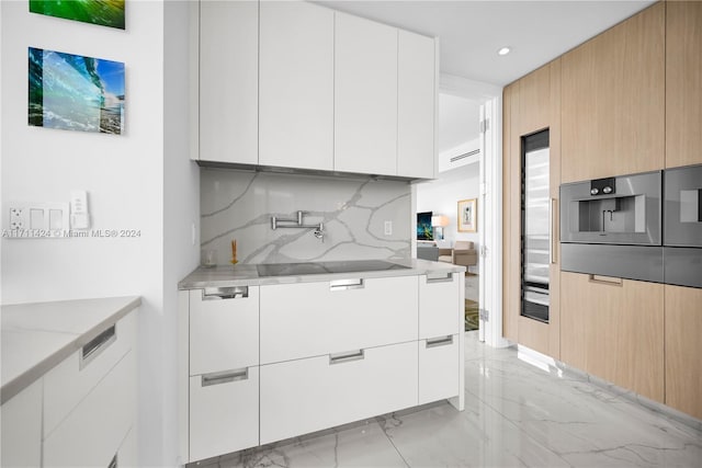 kitchen featuring light stone counters, backsplash, light brown cabinetry, white cabinets, and black stovetop