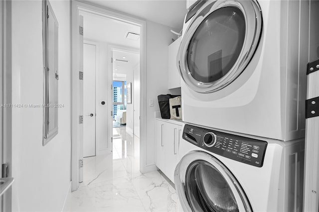 clothes washing area featuring cabinets and stacked washing maching and dryer