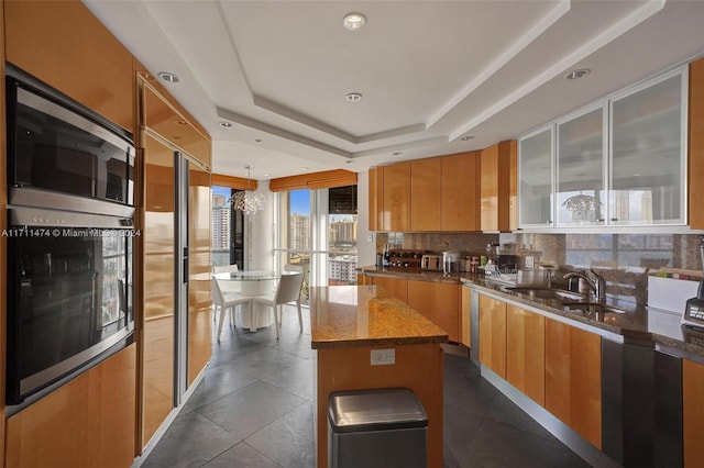 kitchen with decorative backsplash, a center island, a raised ceiling, and sink