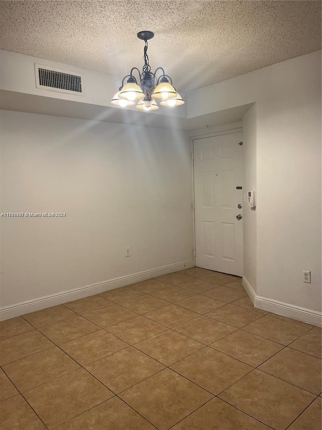 spare room with a chandelier, light tile patterned floors, and a textured ceiling