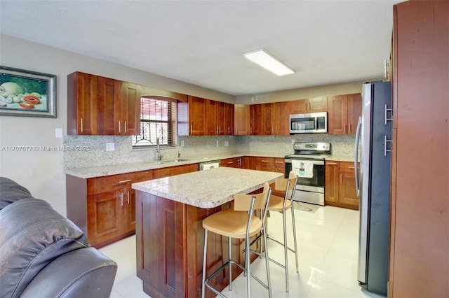 kitchen featuring a kitchen island, appliances with stainless steel finishes, a sink, a kitchen bar, and backsplash