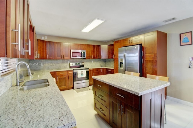 kitchen with light stone countertops, a kitchen island, appliances with stainless steel finishes, and a sink