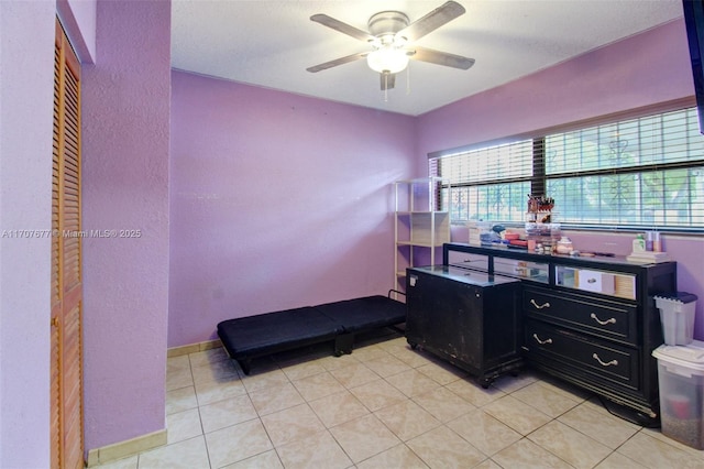 interior space with light tile patterned flooring, a ceiling fan, and baseboards