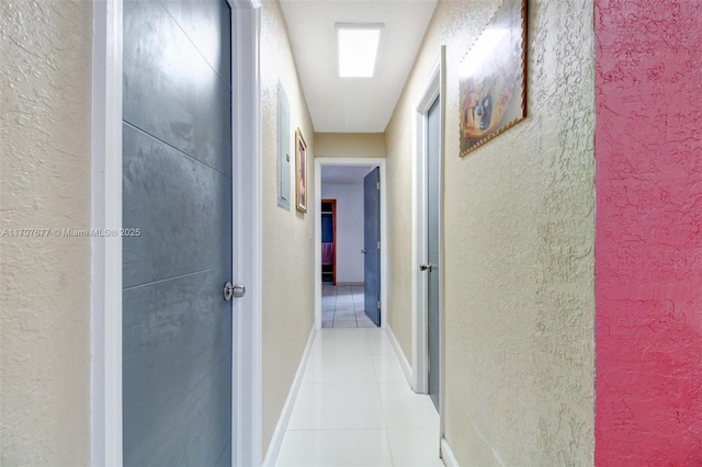 hall featuring light tile patterned flooring, a textured wall, and baseboards