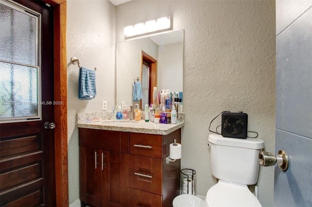 half bathroom featuring toilet, a textured wall, and vanity