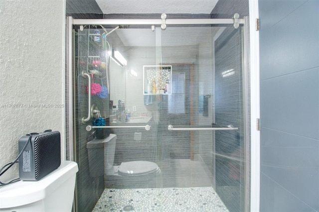 full bath with toilet, a shower stall, and a textured wall