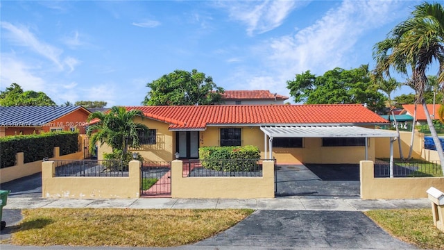 mediterranean / spanish home featuring a fenced front yard, a tiled roof, a gate, a carport, and stucco siding