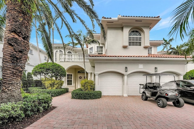 mediterranean / spanish home featuring decorative driveway, a tile roof, stucco siding, a balcony, and a garage