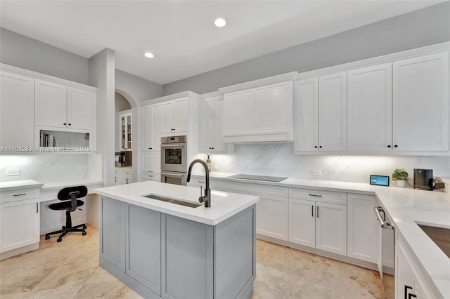 kitchen with arched walkways, a sink, black electric cooktop, double oven, and backsplash