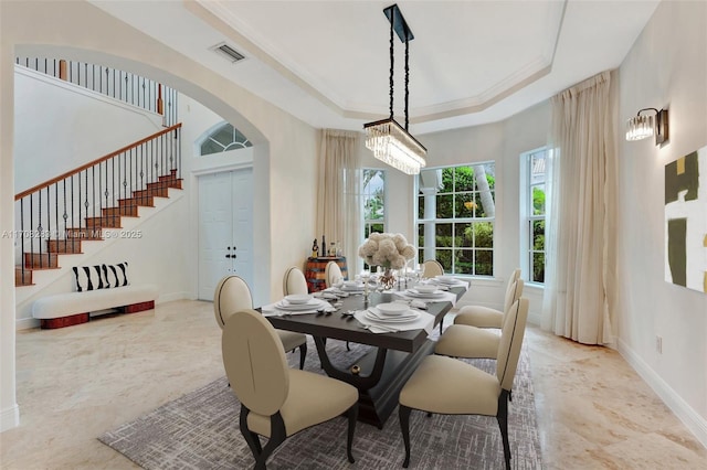 dining room with a tray ceiling, a healthy amount of sunlight, visible vents, and arched walkways