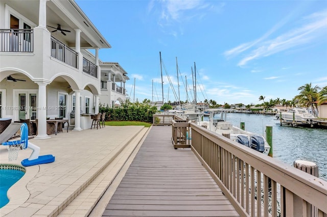 dock area featuring a pool, a patio area, a water view, and a balcony