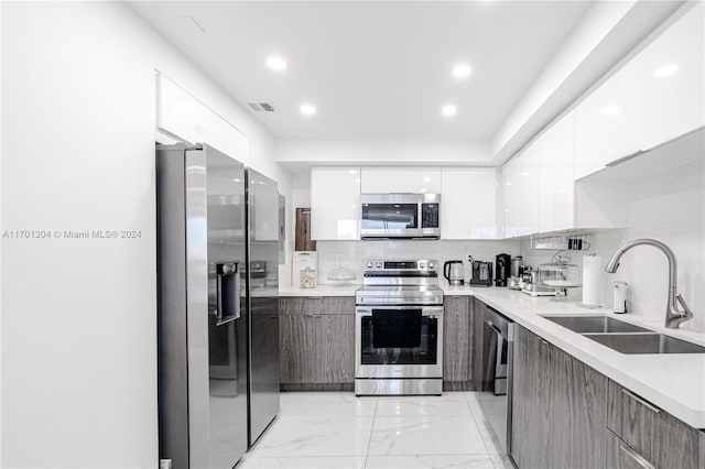 kitchen featuring stainless steel appliances, white cabinetry, tasteful backsplash, and sink