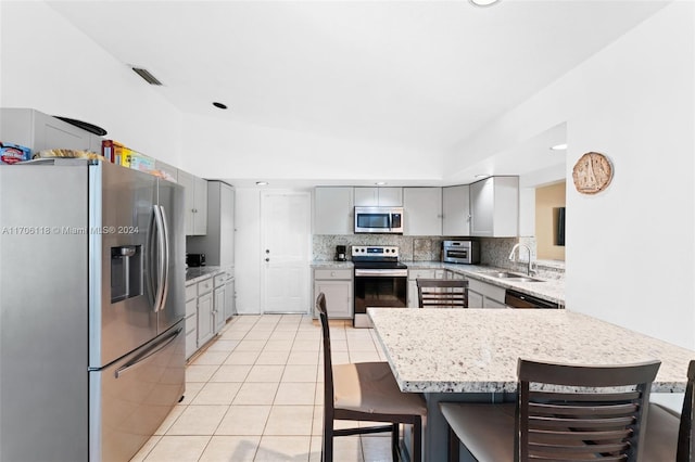 kitchen with kitchen peninsula, appliances with stainless steel finishes, a breakfast bar, and gray cabinetry