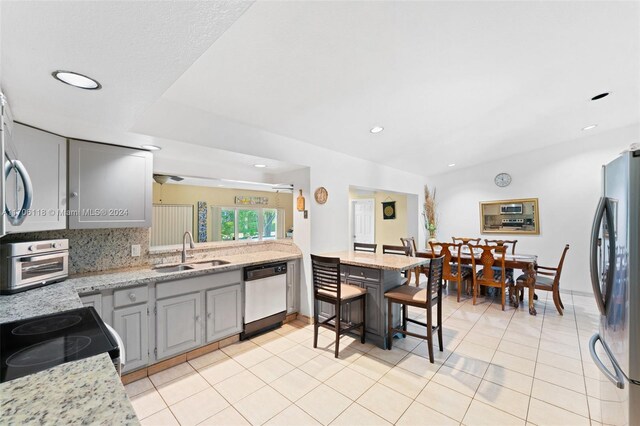 kitchen featuring dishwasher, sink, gray cabinets, light stone counters, and stainless steel refrigerator