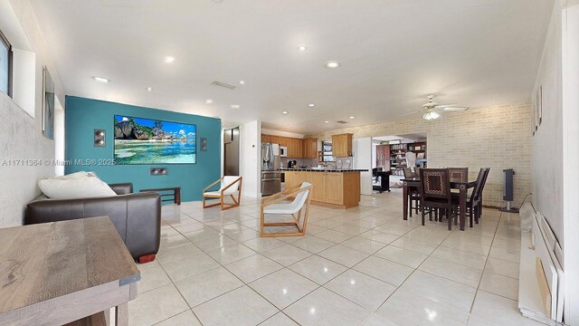 tiled living room with ceiling fan and brick wall