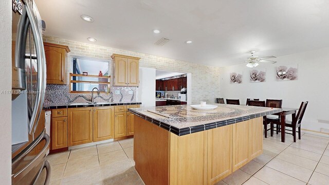 kitchen featuring tile countertops, ceiling fan, tasteful backsplash, stainless steel refrigerator, and a kitchen island