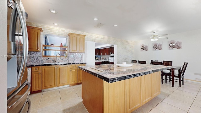 kitchen featuring light tile patterned floors, stainless steel fridge, tasteful backsplash, tile counters, and a kitchen island