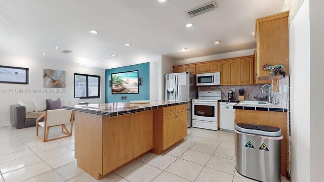 kitchen with backsplash, white appliances, a center island, and tile counters