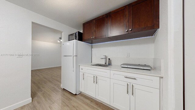 kitchen with ceiling fan, white fridge, sink, white cabinetry, and light wood-type flooring