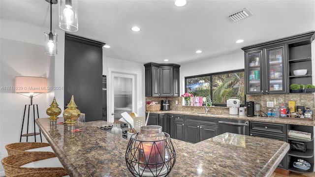 kitchen with dark stone counters, sink, stainless steel dishwasher, decorative backsplash, and a kitchen bar