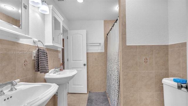 bathroom with tile patterned floors, a shower with curtain, dual sinks, and tile walls