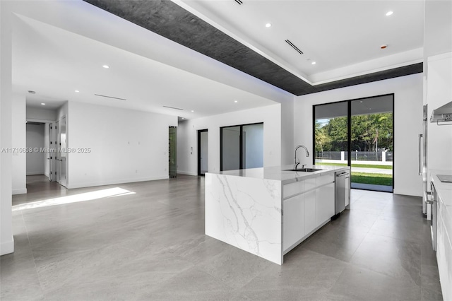 kitchen with sink, a kitchen island with sink, light stone countertops, white cabinets, and stainless steel dishwasher