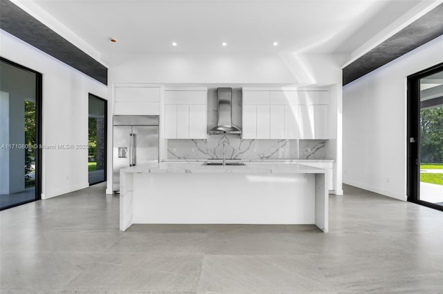 kitchen with white cabinetry, stainless steel built in refrigerator, backsplash, wall chimney exhaust hood, and a spacious island