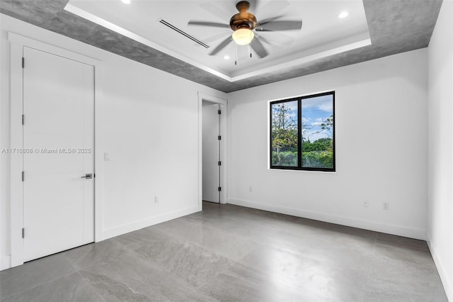 empty room with ceiling fan and a tray ceiling