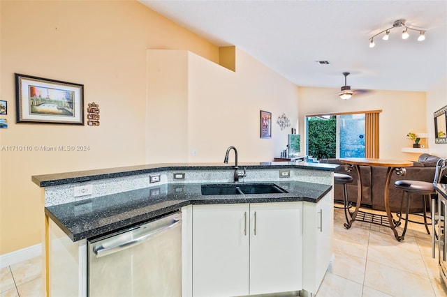 kitchen with white cabinets, dark stone counters, vaulted ceiling, sink, and dishwasher