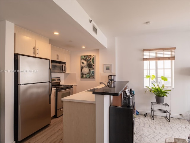 kitchen featuring sink, kitchen peninsula, stainless steel appliances, and light hardwood / wood-style flooring