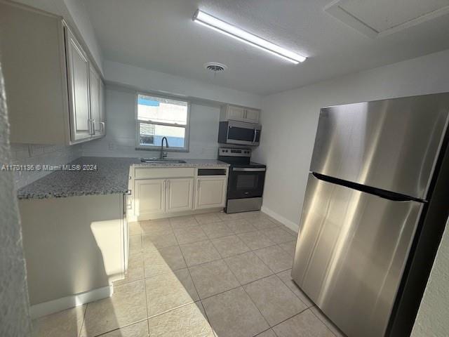 kitchen featuring sink, light stone countertops, light tile patterned flooring, white cabinetry, and stainless steel appliances