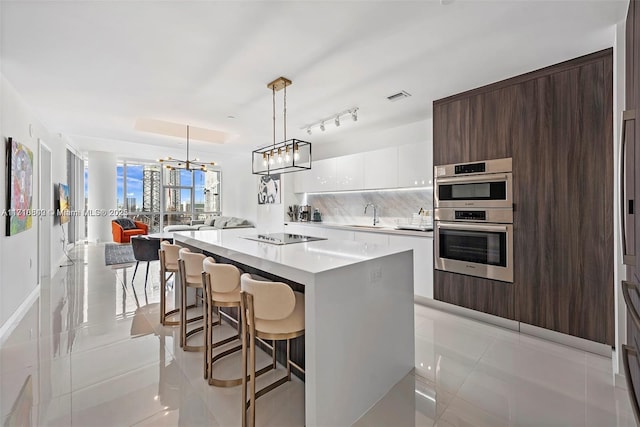 kitchen with decorative light fixtures, dark brown cabinets, a kitchen island, white cabinets, and backsplash