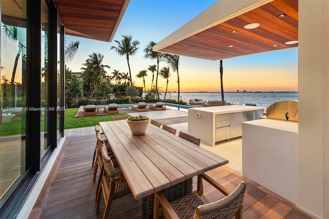 patio terrace at dusk with area for grilling, a water view, and exterior kitchen