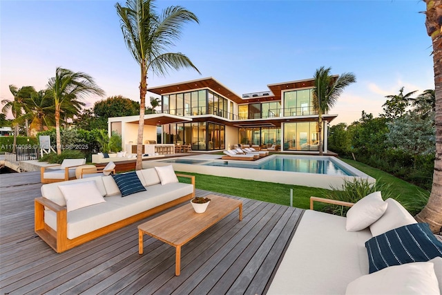 back house at dusk featuring an outdoor living space, a balcony, and a swimming pool side deck