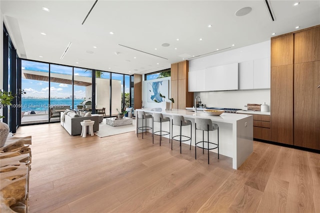 kitchen with floor to ceiling windows, a large island with sink, a water view, light hardwood / wood-style flooring, and white cabinetry