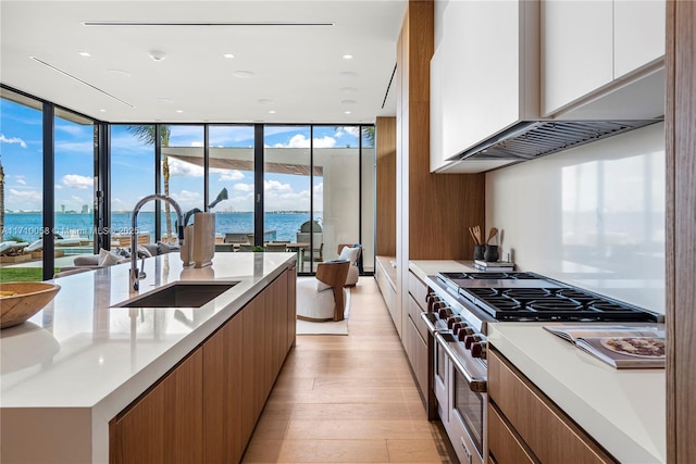 kitchen featuring range with two ovens, a water view, sink, wall chimney range hood, and white cabinetry