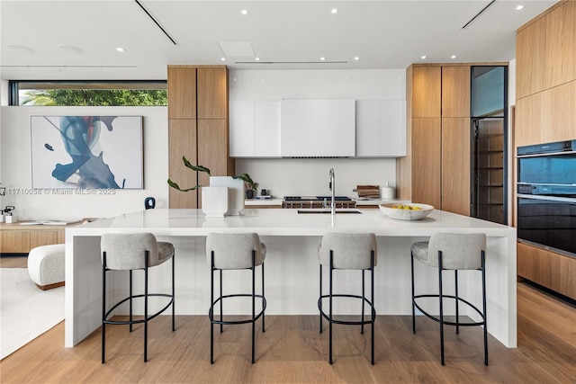 kitchen with a kitchen bar, light wood-type flooring, black double oven, and white cabinetry